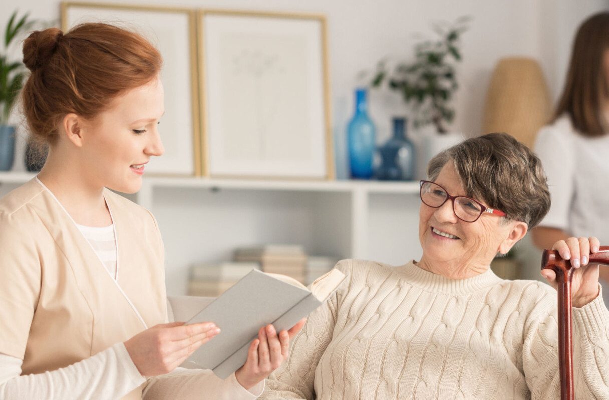 Nurse,Reading,To,An,Elderly,Woman,With,A,Cane,And Omasuuntima
